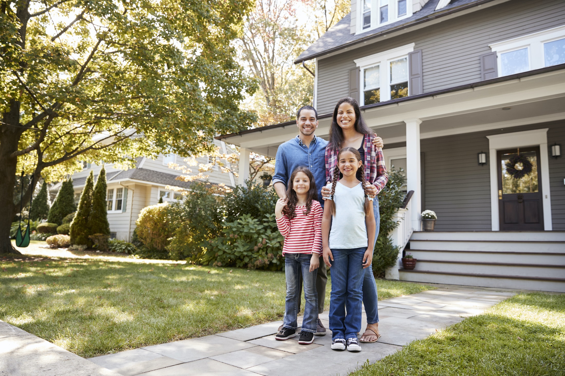 A happy family of four standing outside their suburban home on a sunny day.
