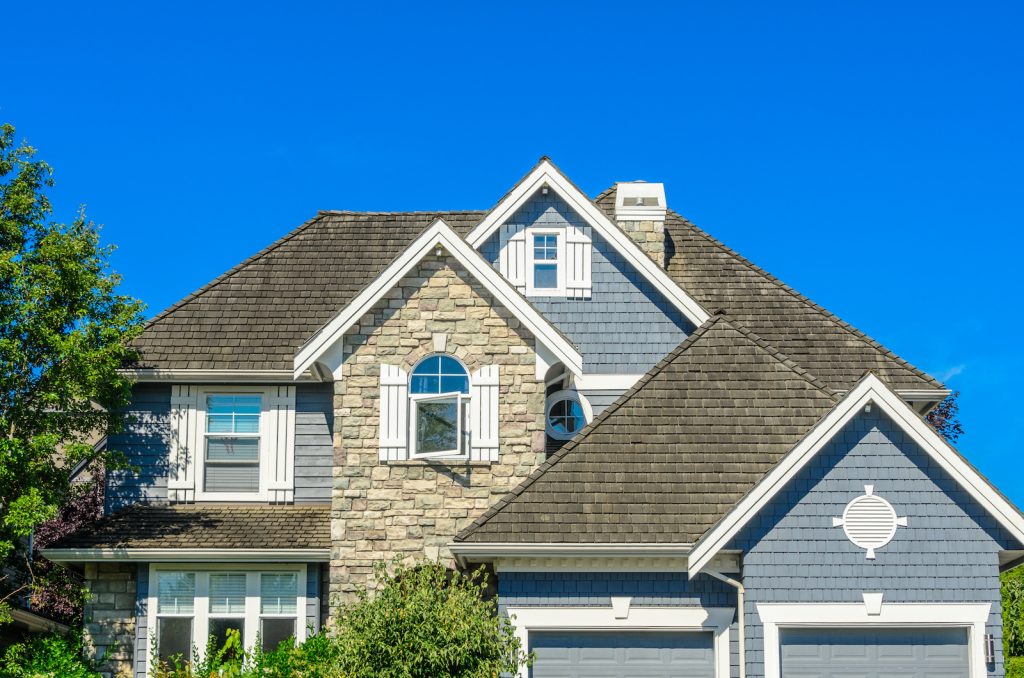 A beautiful suburban house with stone and blue siding under a clear blue sky.