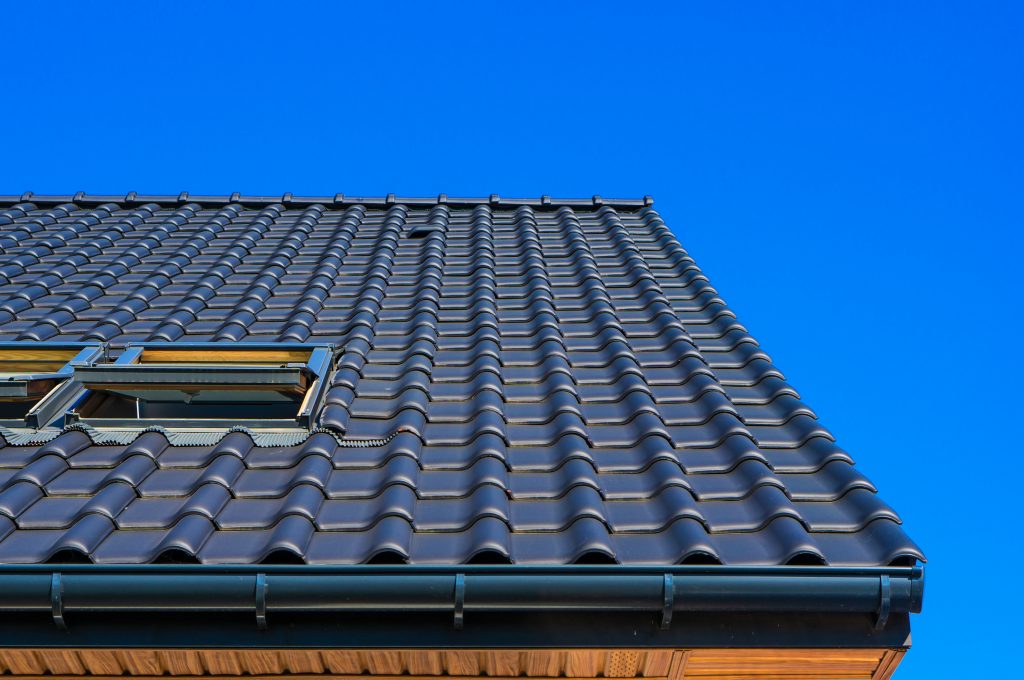 Close-up of a roof with dark blue tiles under a bright blue sky.